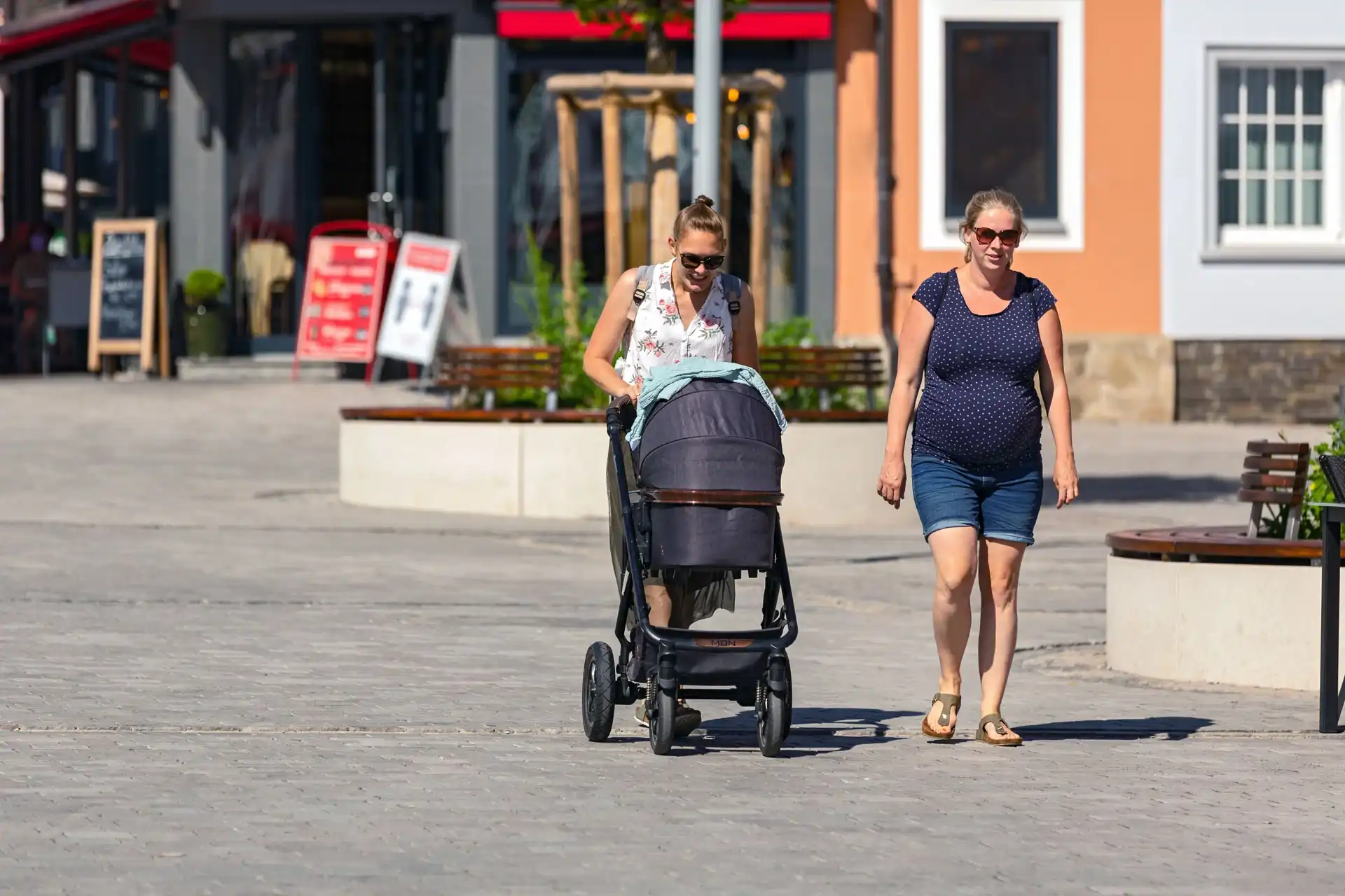Eine Frau spaziert zusammen mit ihrer schwangeren Freundin über den neuen Marktplatz in Wipperfürth und schiebt einen Kinderwagen vor sich her.
