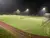 Beleuchteter Fußballplatz bei Nacht mit Spielern in Aktion und Zuschauern im Hintergrund