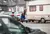 Ein Mann mit einem Hut schiebt einem Wohnwagen in einer Stadt, umgeben von parkenden Autos.
