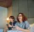 Zwei Jugendliche spielen Videospiele auf einem Bett und lachen dabei in einem modernen Zimmer.
